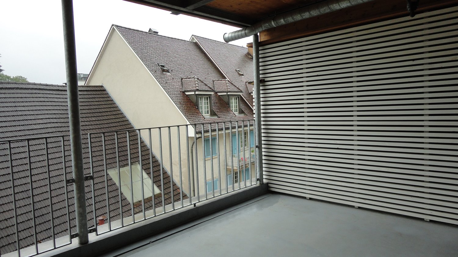 metal railing, concrete floor, closed white wooden louvered wall, visible exterior of other buildings