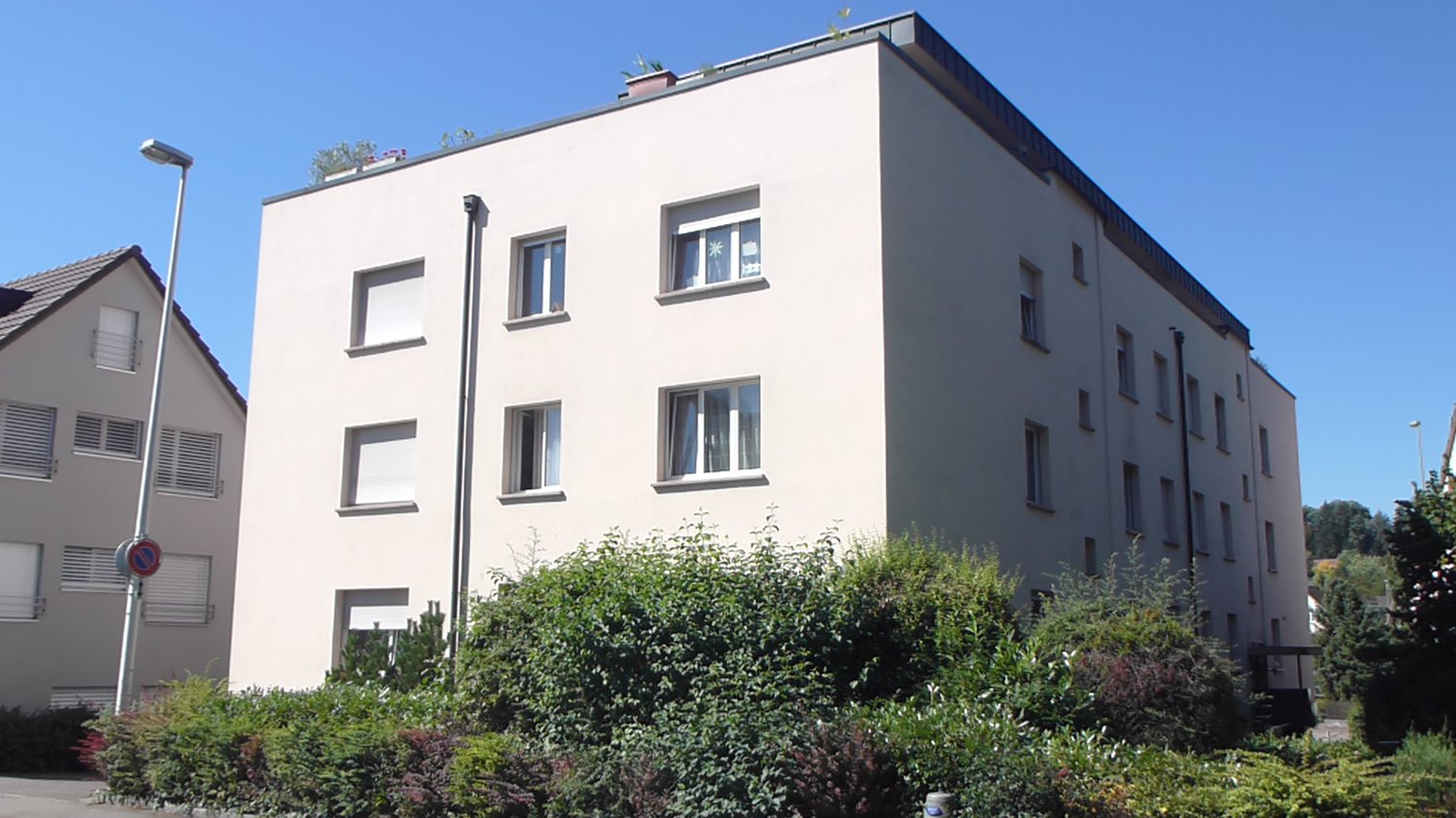 3 story white building, multiple windows, shrubs in front, street light