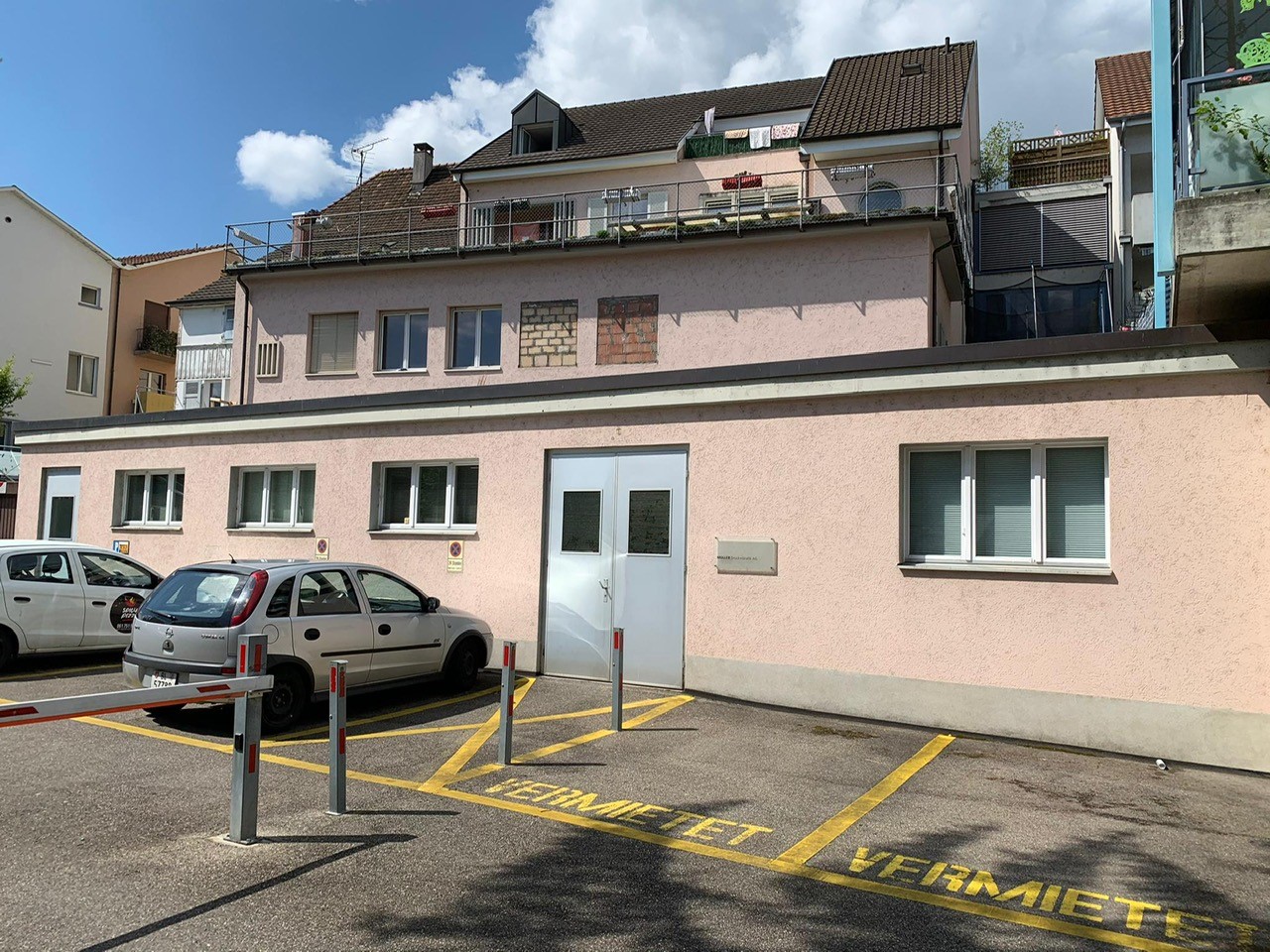 apartment building, multiple floors, 2 cars parked, grey metal poles in parking lot