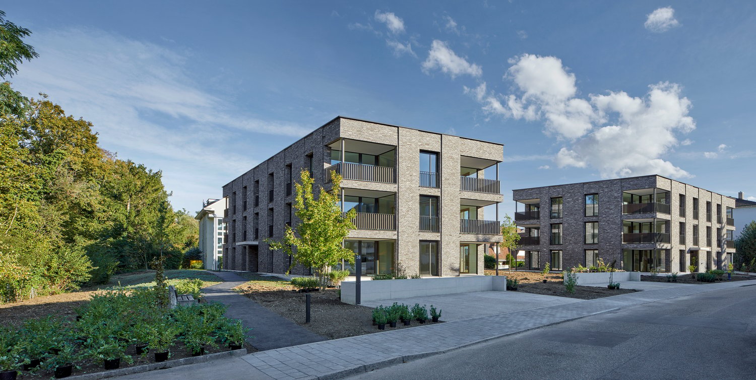 Modern apartment building, brick facade, multiple balconies, landscaped garden, paved walkway