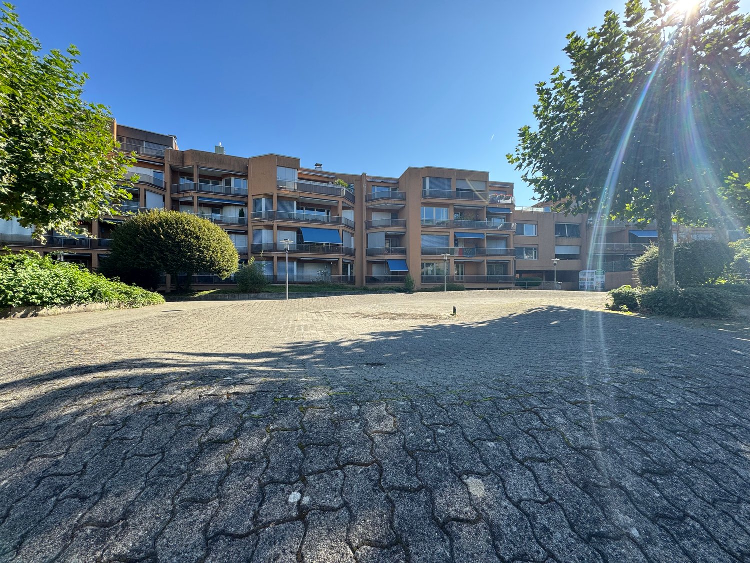 multi-story building with parking area, brick facade, balconies, trees, streetlights
