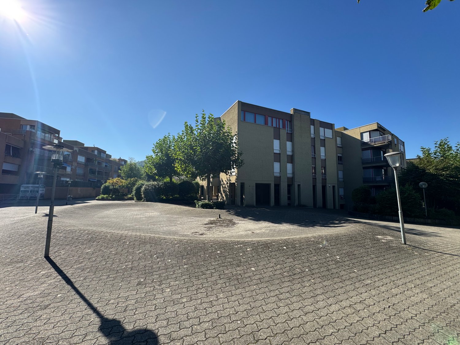 Building exterior, paved parking lot, street lights, surrounding buildings, trees, bushes