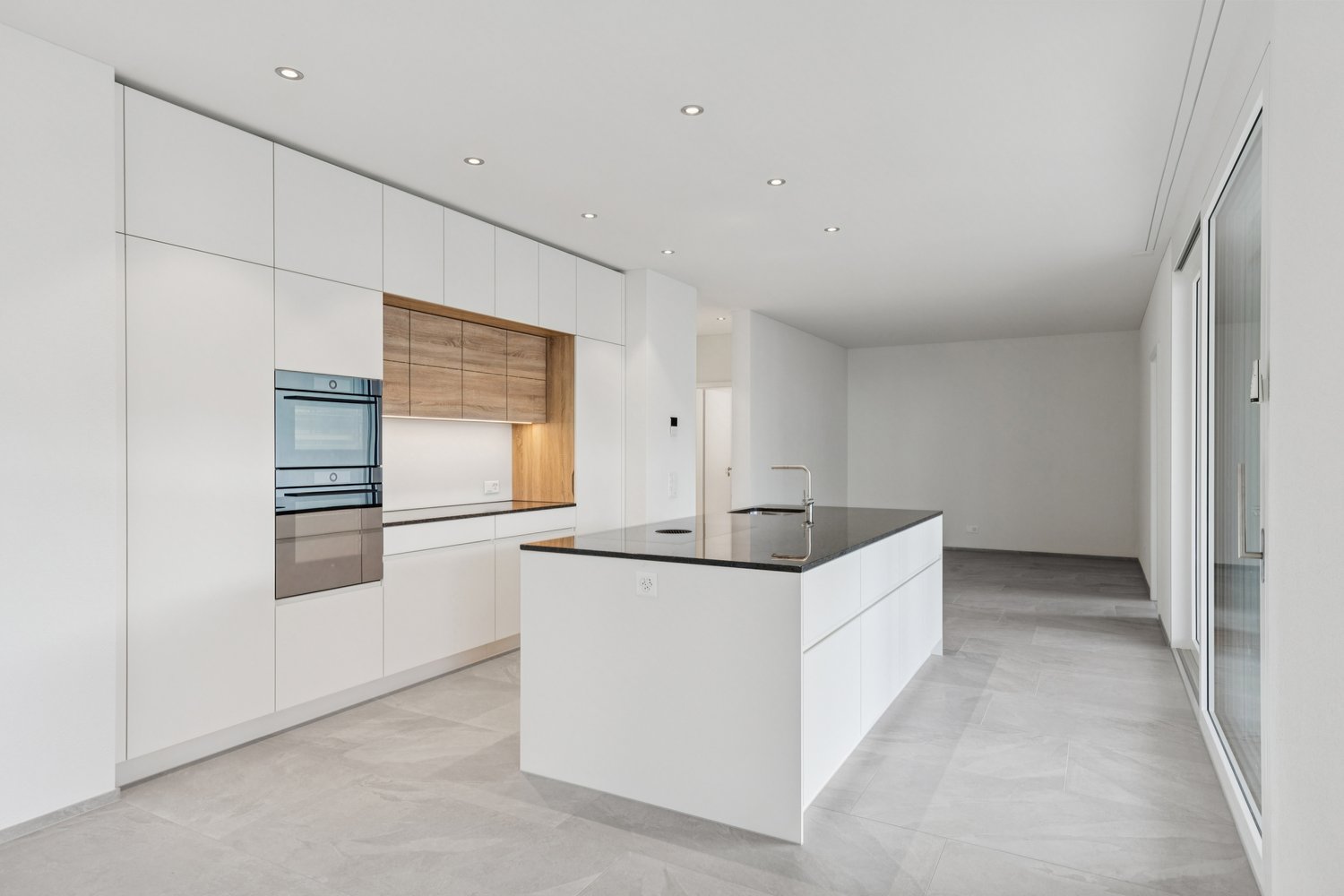 Modern kitchen with white cabinetry, black countertop, integrated appliances, and a large sink with a faucet.