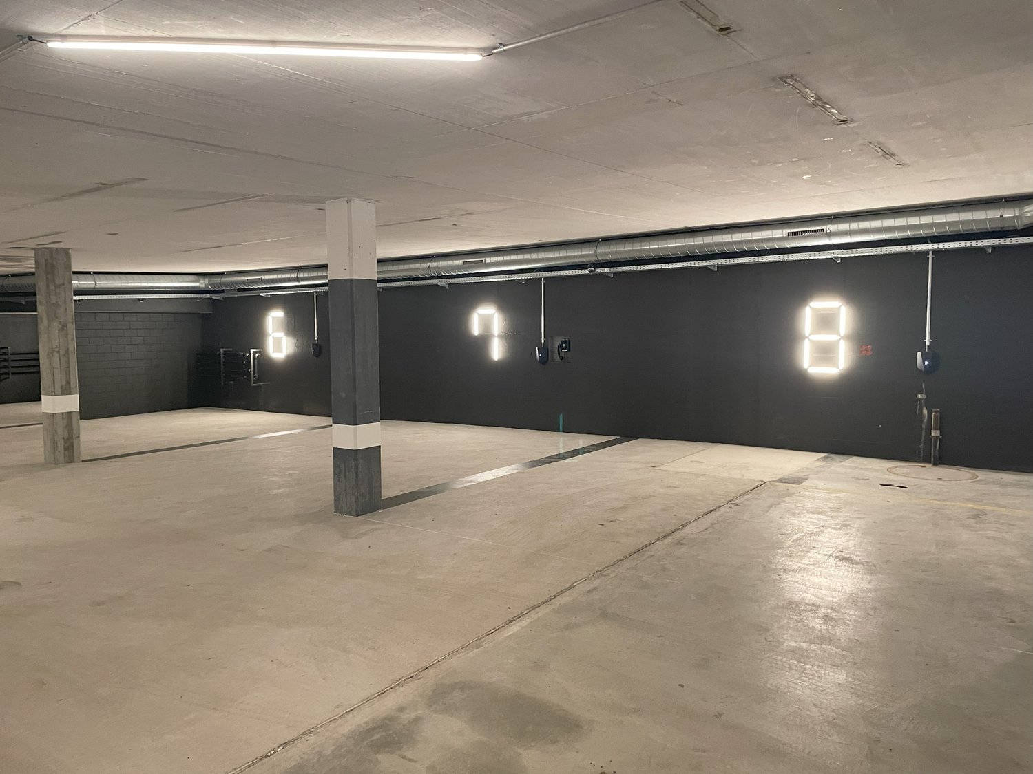 Large open parking garage with concrete floor, concrete columns, and overhead lighting