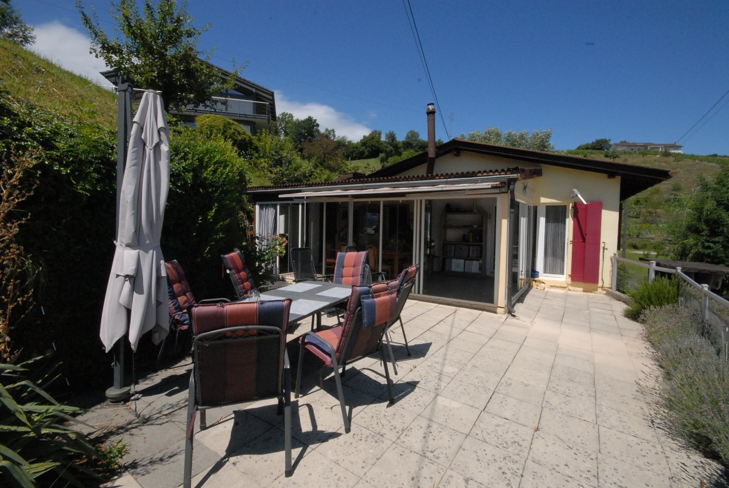 House with a patio, outdoor dining table, chairs, and an umbrella. Fireplace and shelves visible inside.
