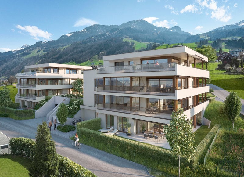 Multi-story apartment building with balconies, surrounded by green landscaping and with a scenic mountain backdrop