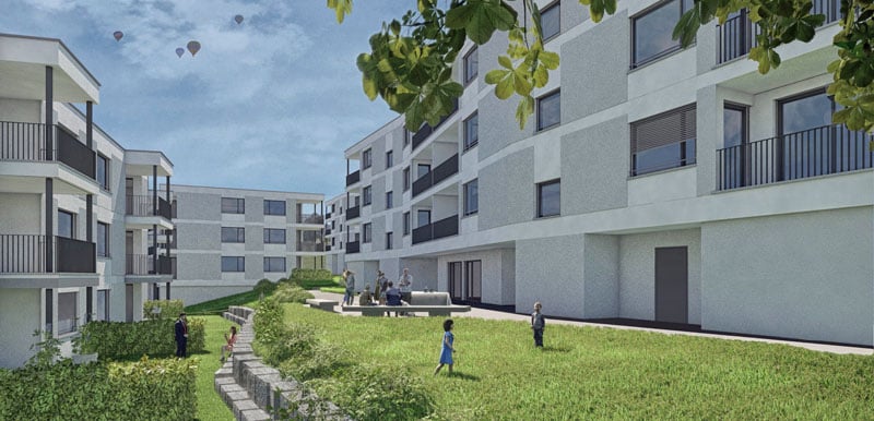 Multi-story apartment building with balconies, surrounded by a grassy courtyard with walkways and benches. The building has a modern, minimalist design with large windows.