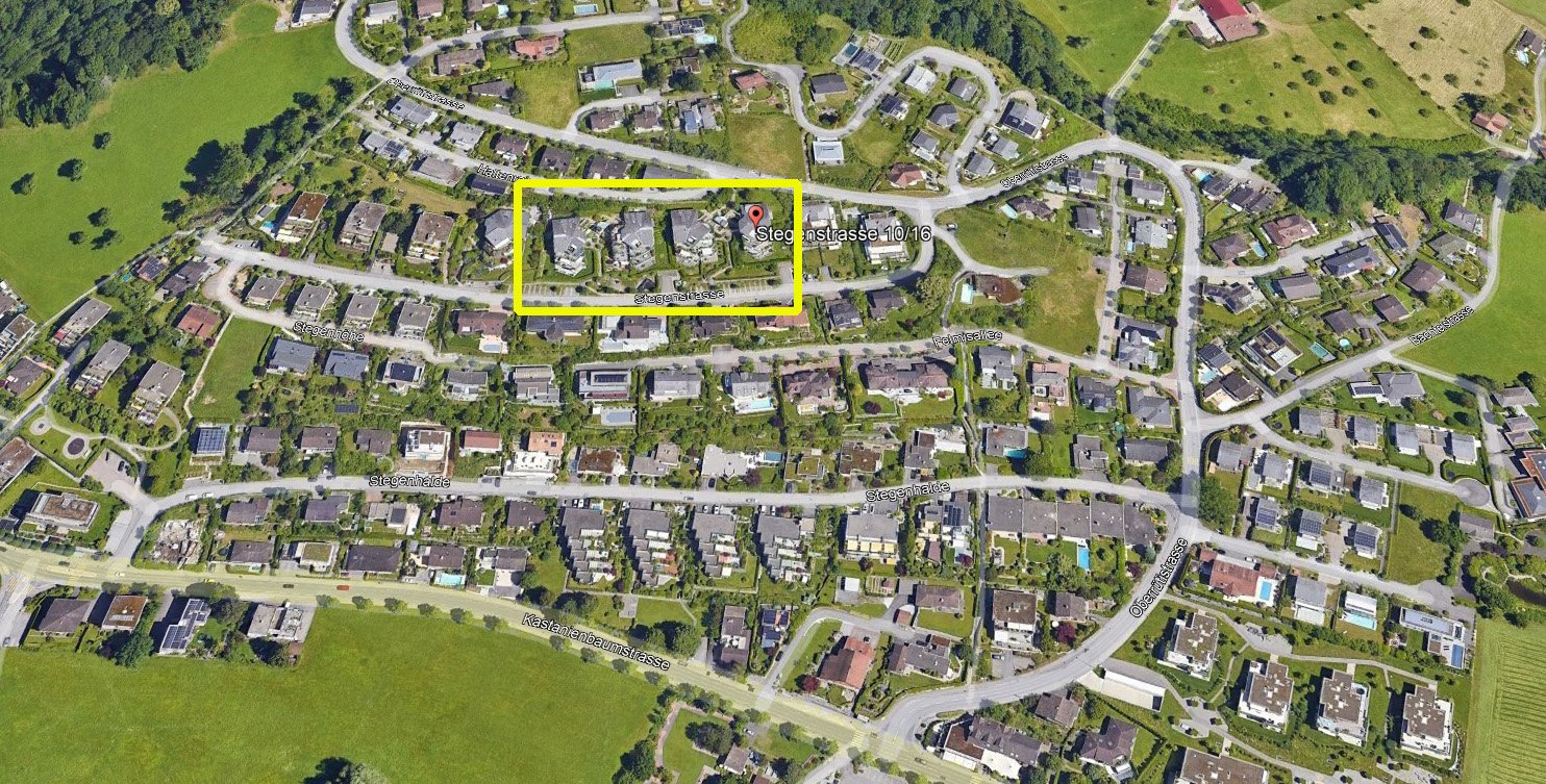 Top-down aerial view of residential neighborhood with various houses, roads, green spaces, and some trees