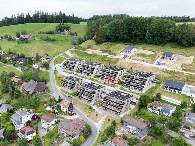 Cluster of buildings with solar panels on roofs, surrounded by greenery, various buildings in different sizes and styles