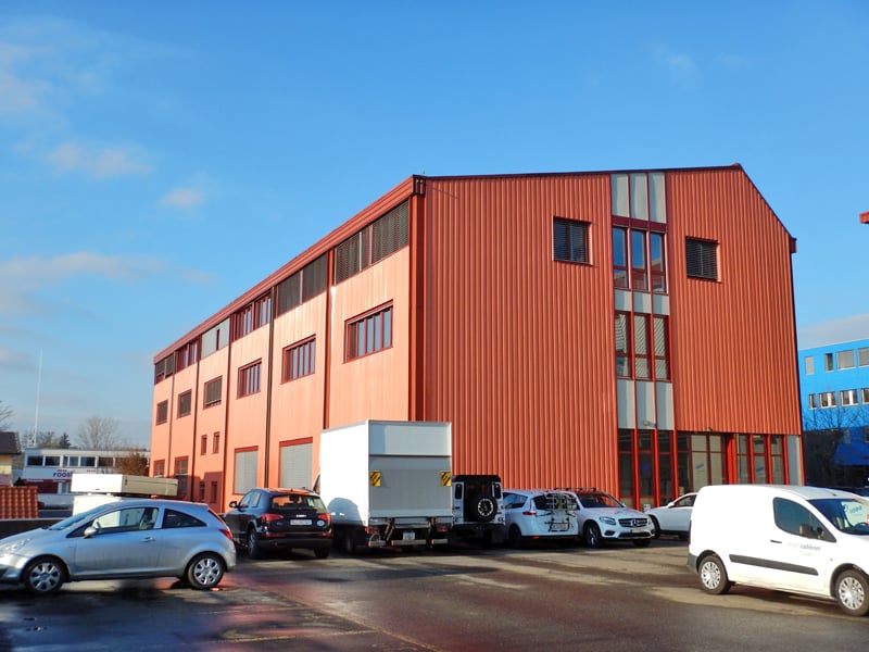 Warehouse building, multiple windows, red and blue exterior, several cars parked in front