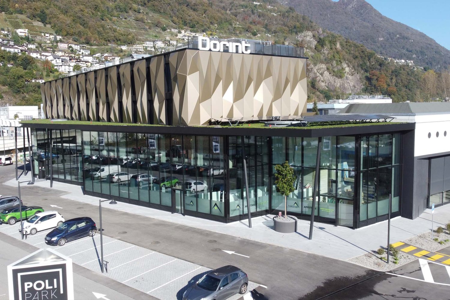 modern building with glass facade, large parking lot, several parked cars, mountains in the background