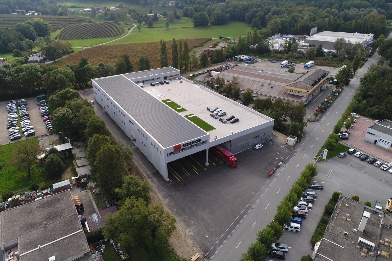 large industrial building with loading dock and parking spaces in front, several other buildings and cars parked in the background