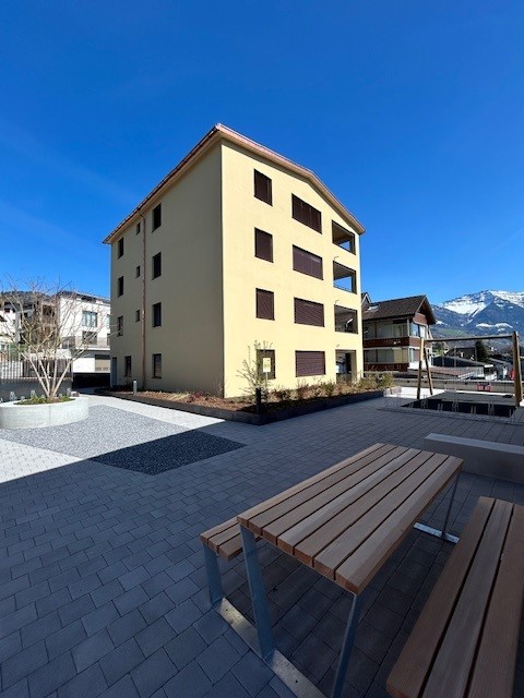 A yellow building with multiple windows, a playground, and a bench in front of it.