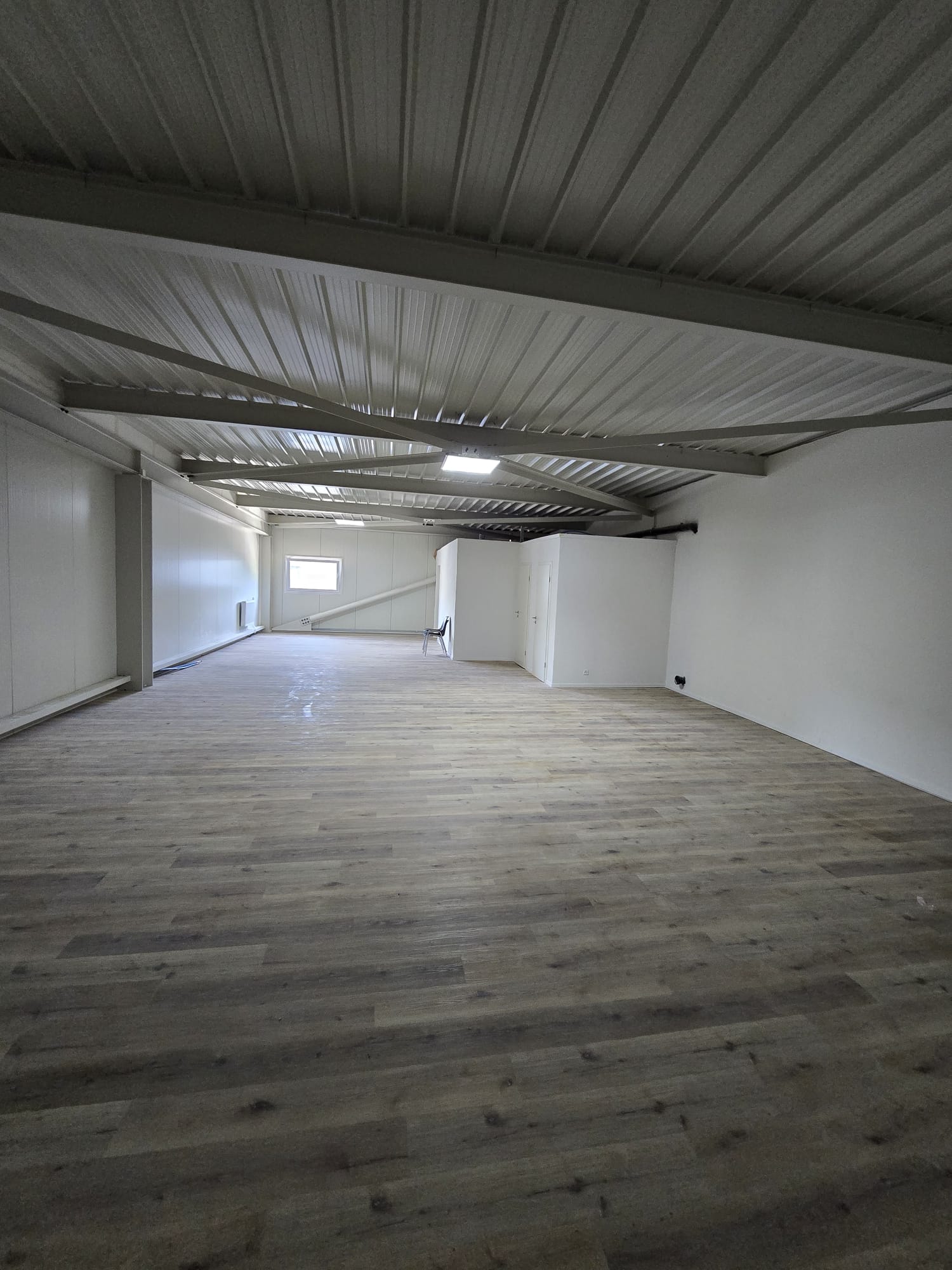 large open room, wooden floors, white walls, metal ceiling, small window