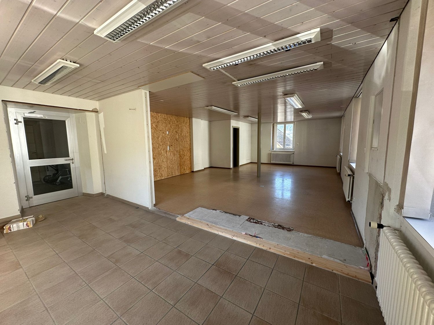 Empty room with tiled floor, white walls, wooden ceiling, and multiple windows.