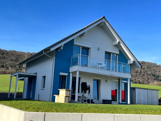 Two-story modern house with white exterior and blue accents, large windows, balcony, and attached garage.