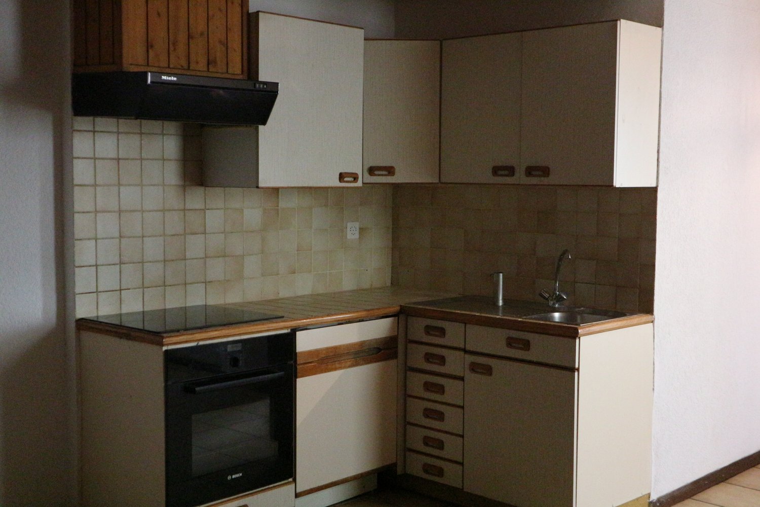 Compact kitchen with wooden cabinets, tile backsplash, black appliances including a dishwasher, and a sink with a faucet