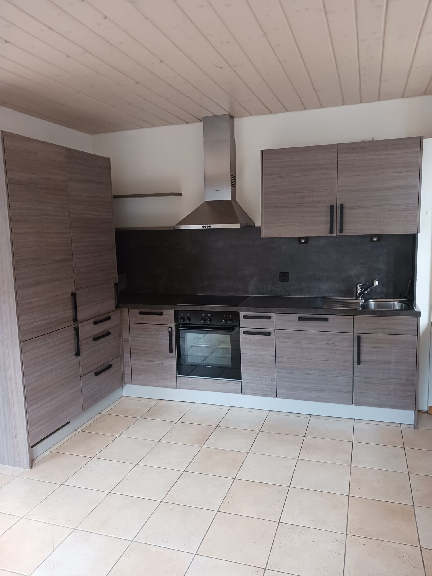 Modern kitchen with gray wood-paneled cabinets, black countertops, built-in oven and stove, and a dishwasher.