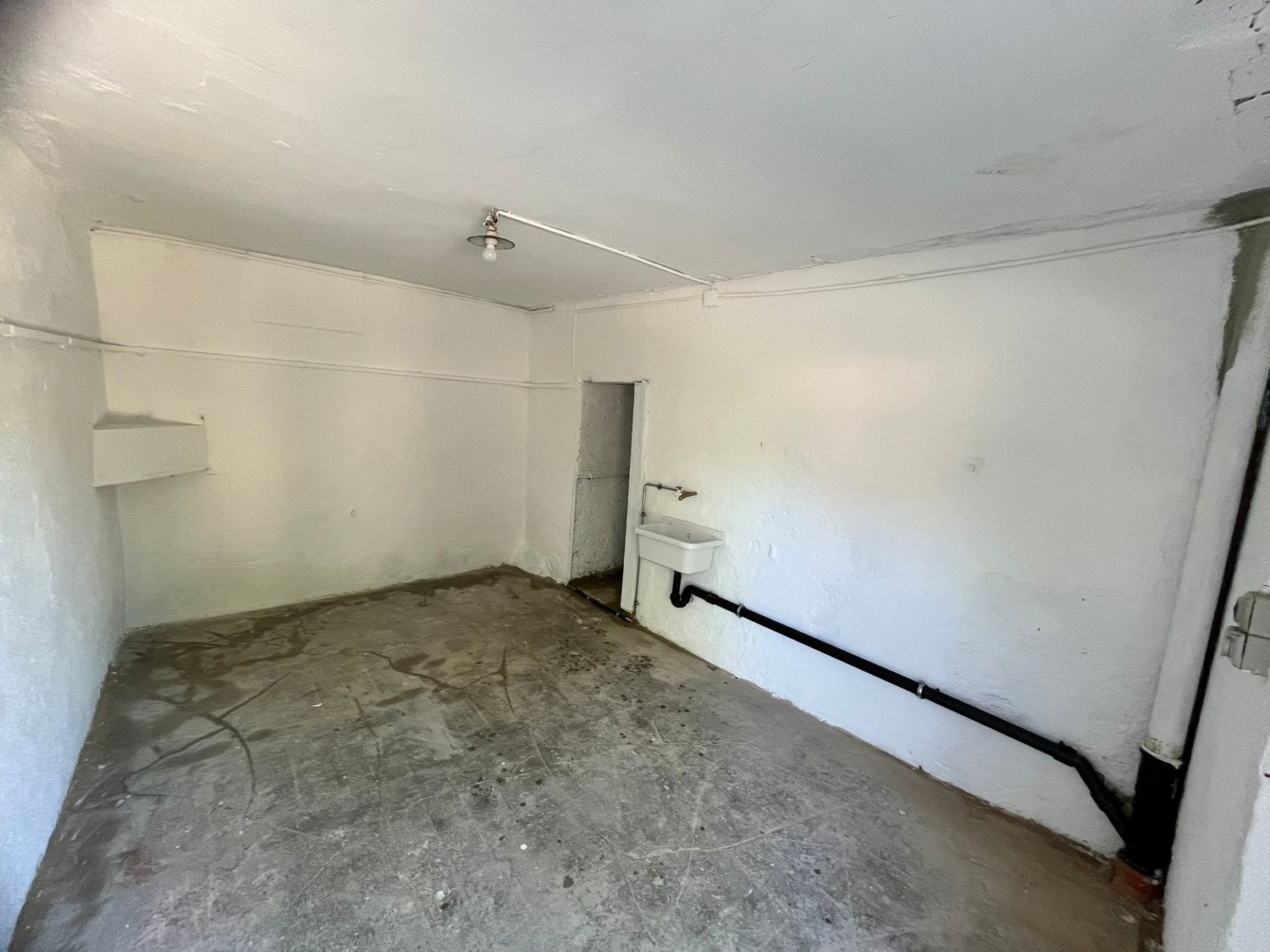 Unfinished basement or storage room with concrete floor, white walls, and a utility sink or basin on the wall.