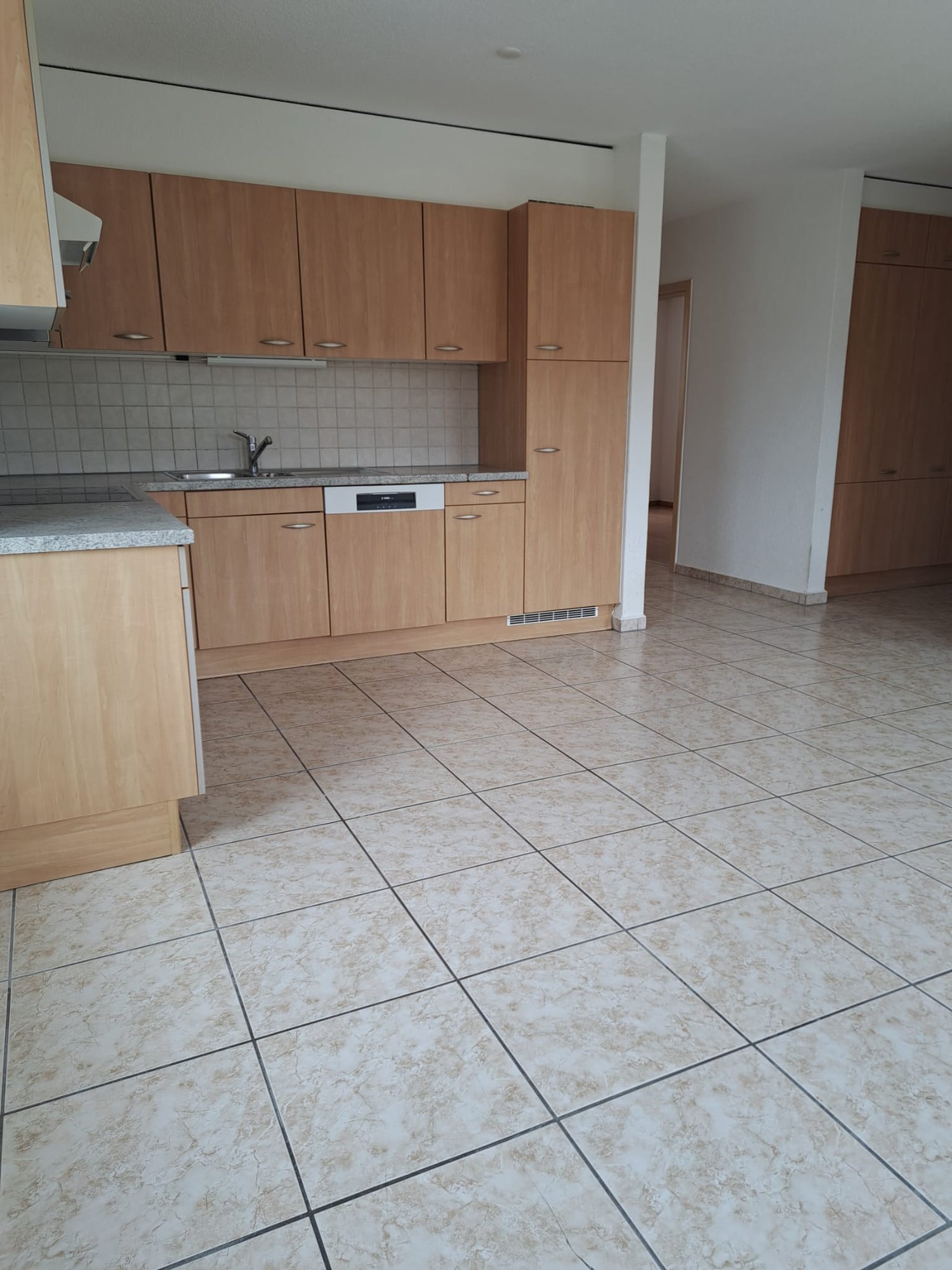 empty kitchen with wooden cabinets, tiled flooring, stainless steel sink, dishwasher