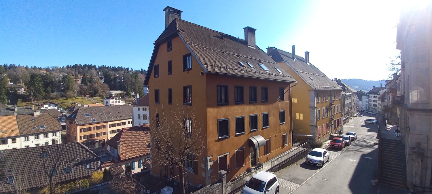 3 story house, brown roof, multiple windows, cars parked on street