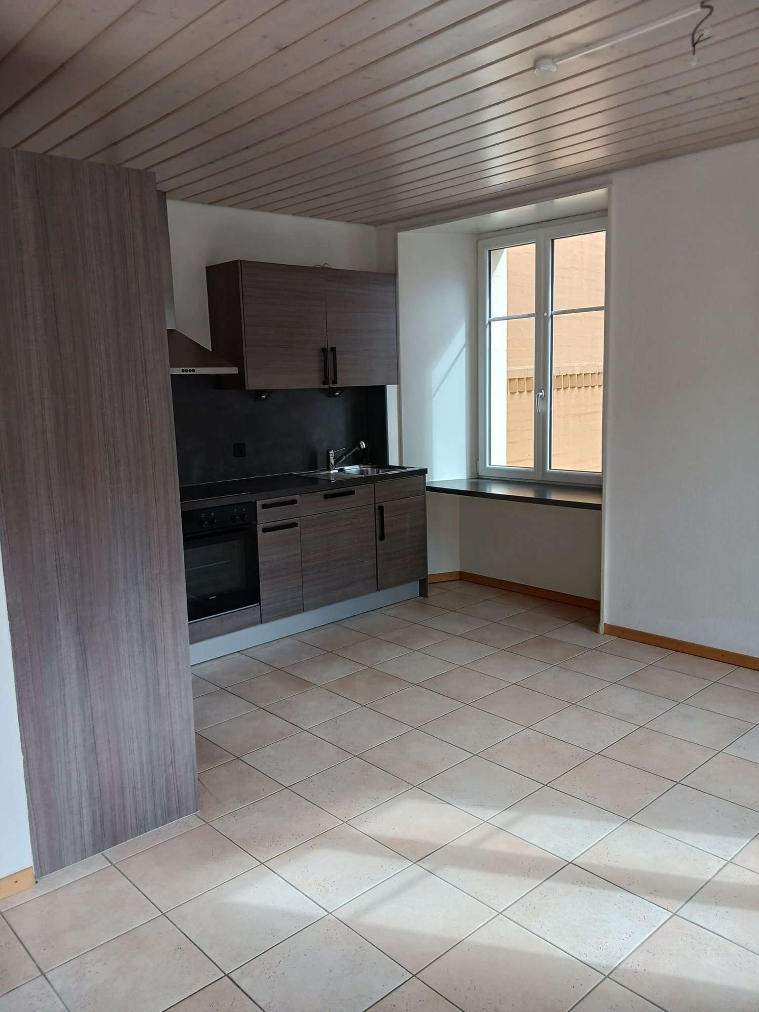 empty kitchen with tiled floor, wooden cabinets, black countertop, sink, oven, window