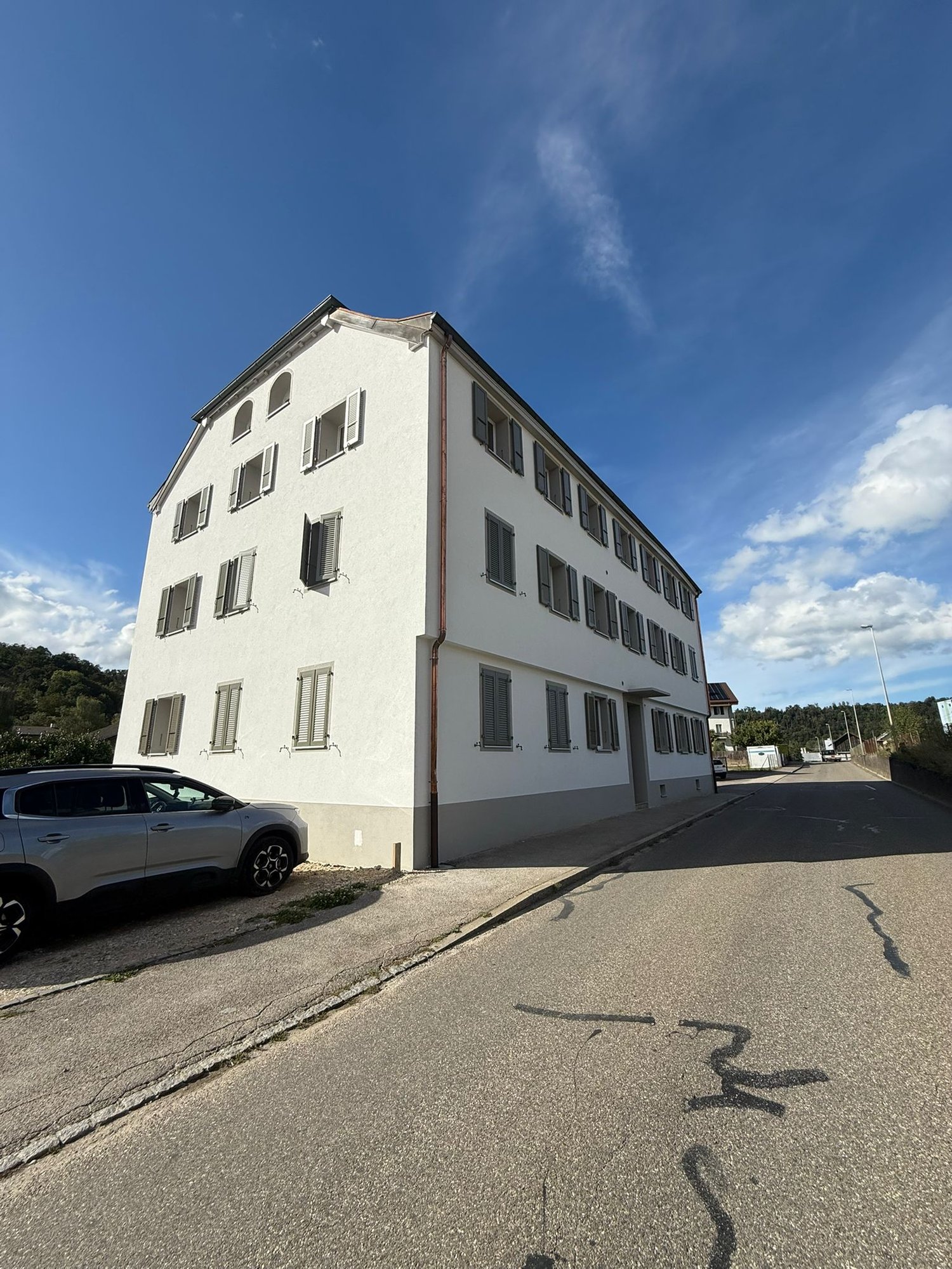 white residential building, several floors, multiple windows, car parked in front