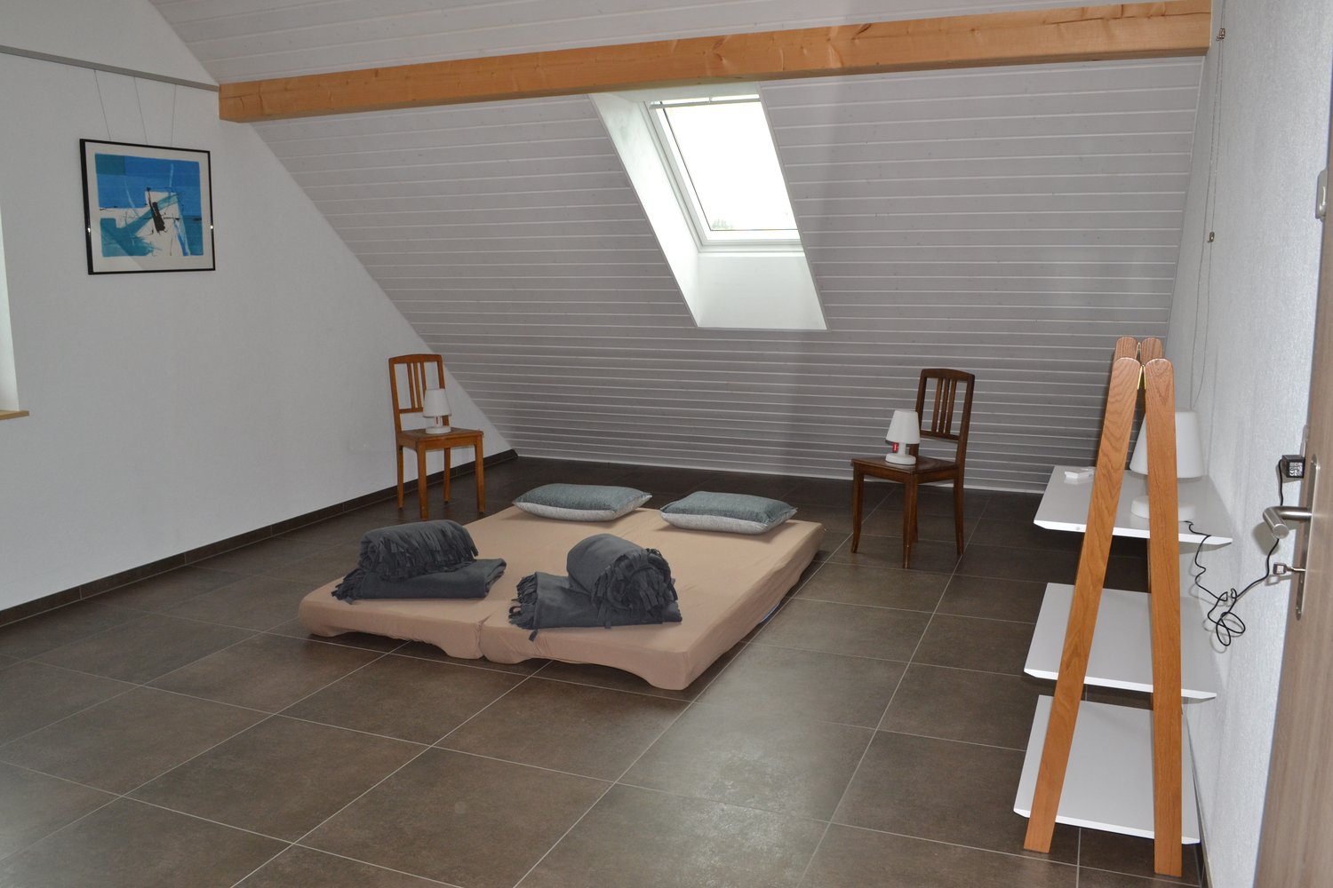 Attic bedroom with slanted ceiling, large window, hardwood floors, wooden beams, and a bed with gray bedding