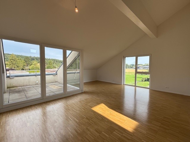 Spacious living room with hardwood floors, large windows providing natural light and access to a balcony or terrace, high ceilings, and an open layout.