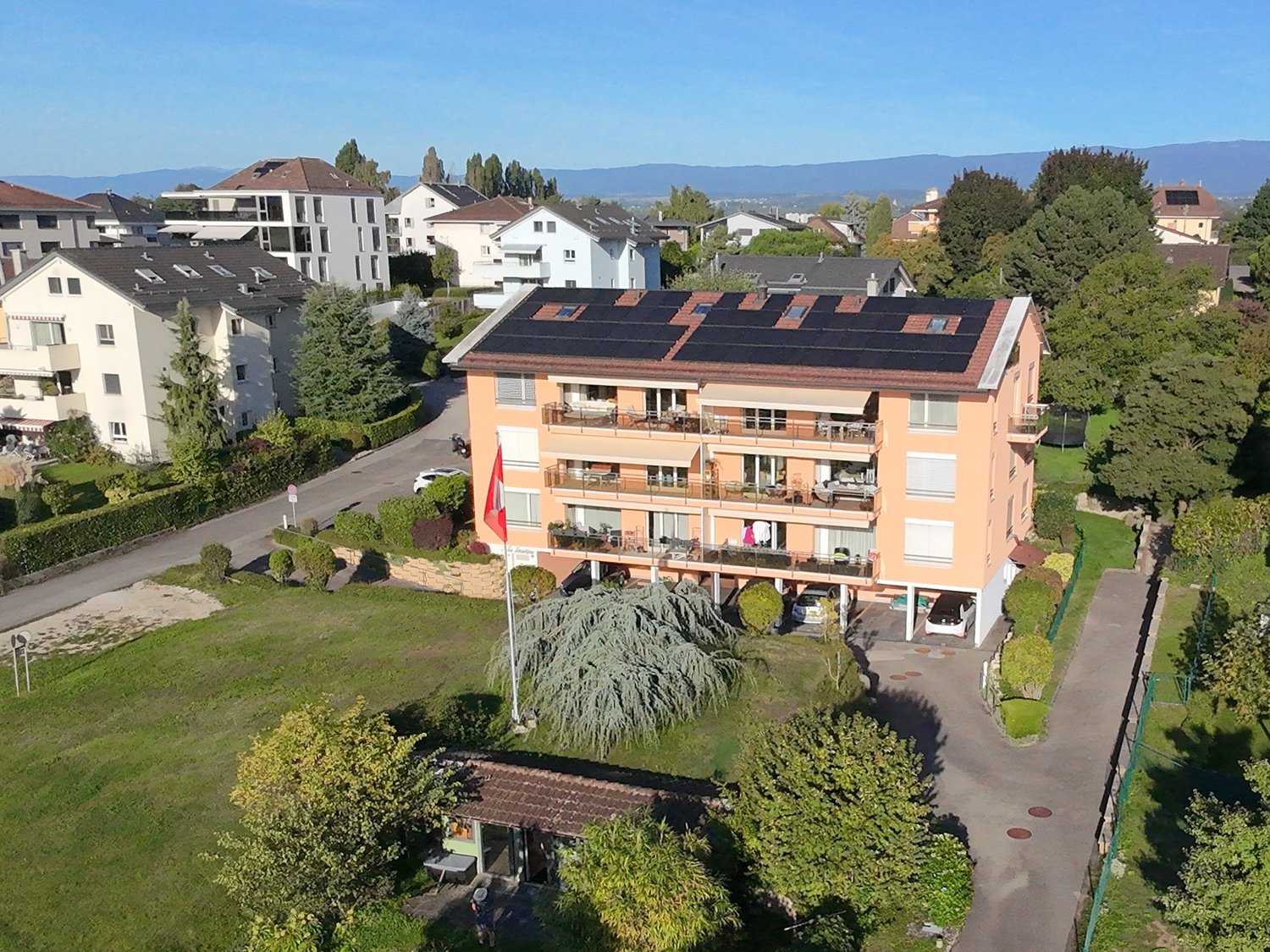 3 story apartment building with solar panels on the roof, balconies on each floor, car parking area in front