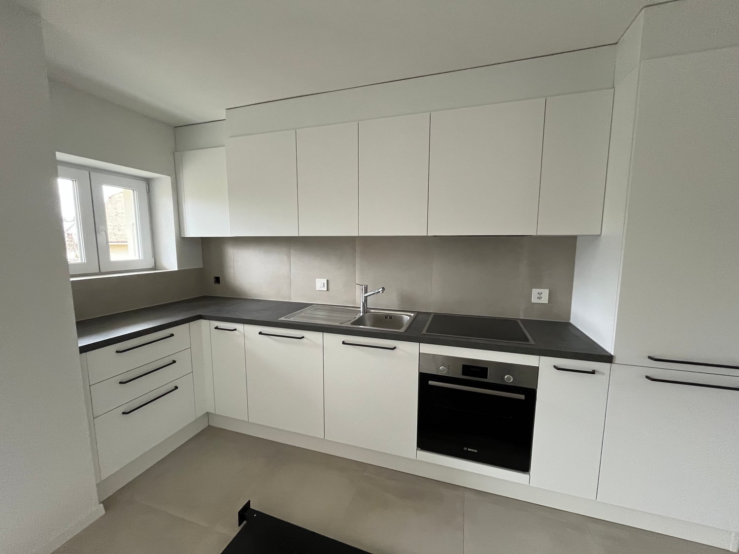 kitchen with white cabinets, black countertops, stainless steel sink, faucet, oven, integrated appliances, windows