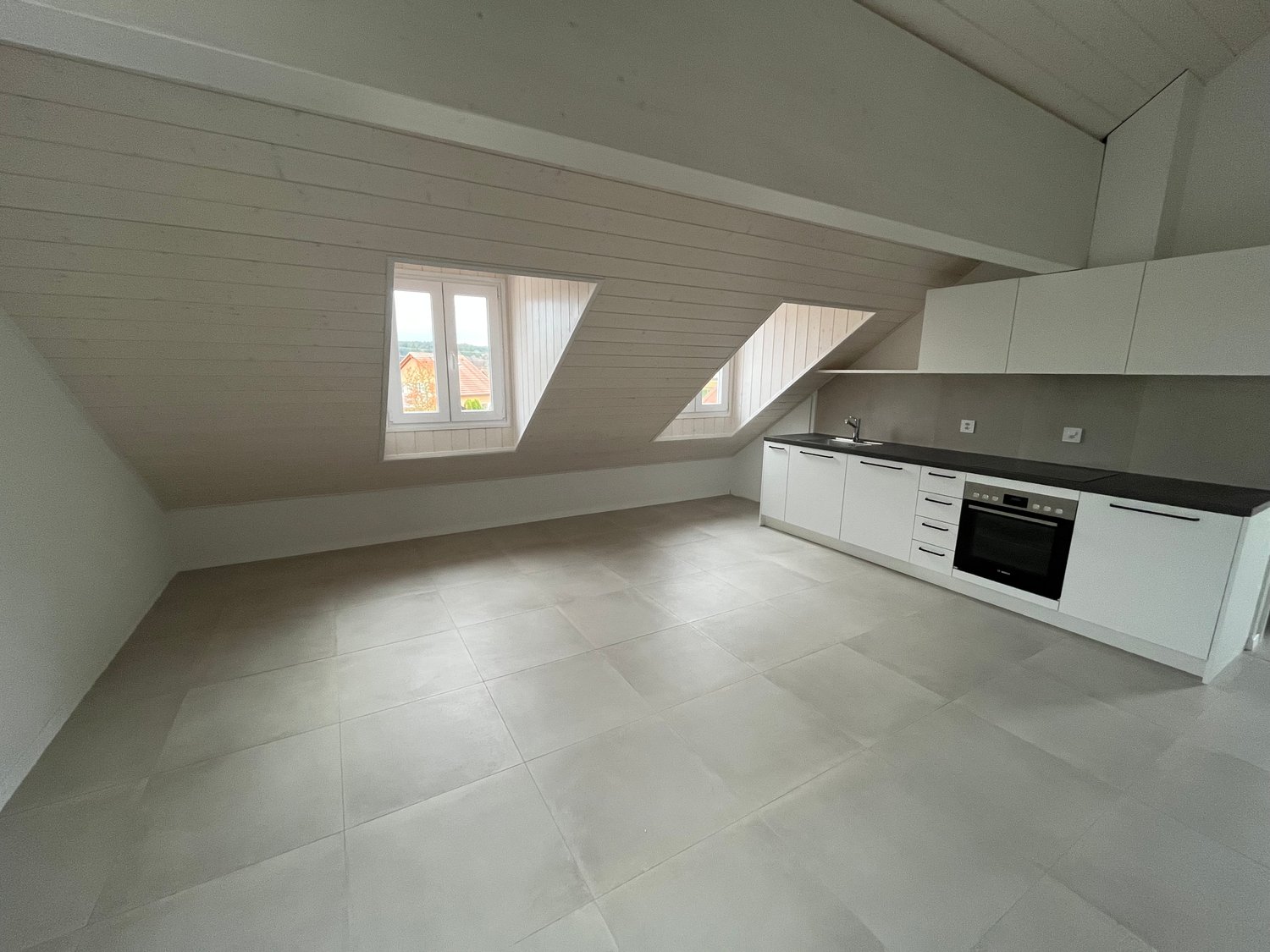 empty kitchen, white tiled floor, black countertops, white cabinets, white oven, two triangular windows