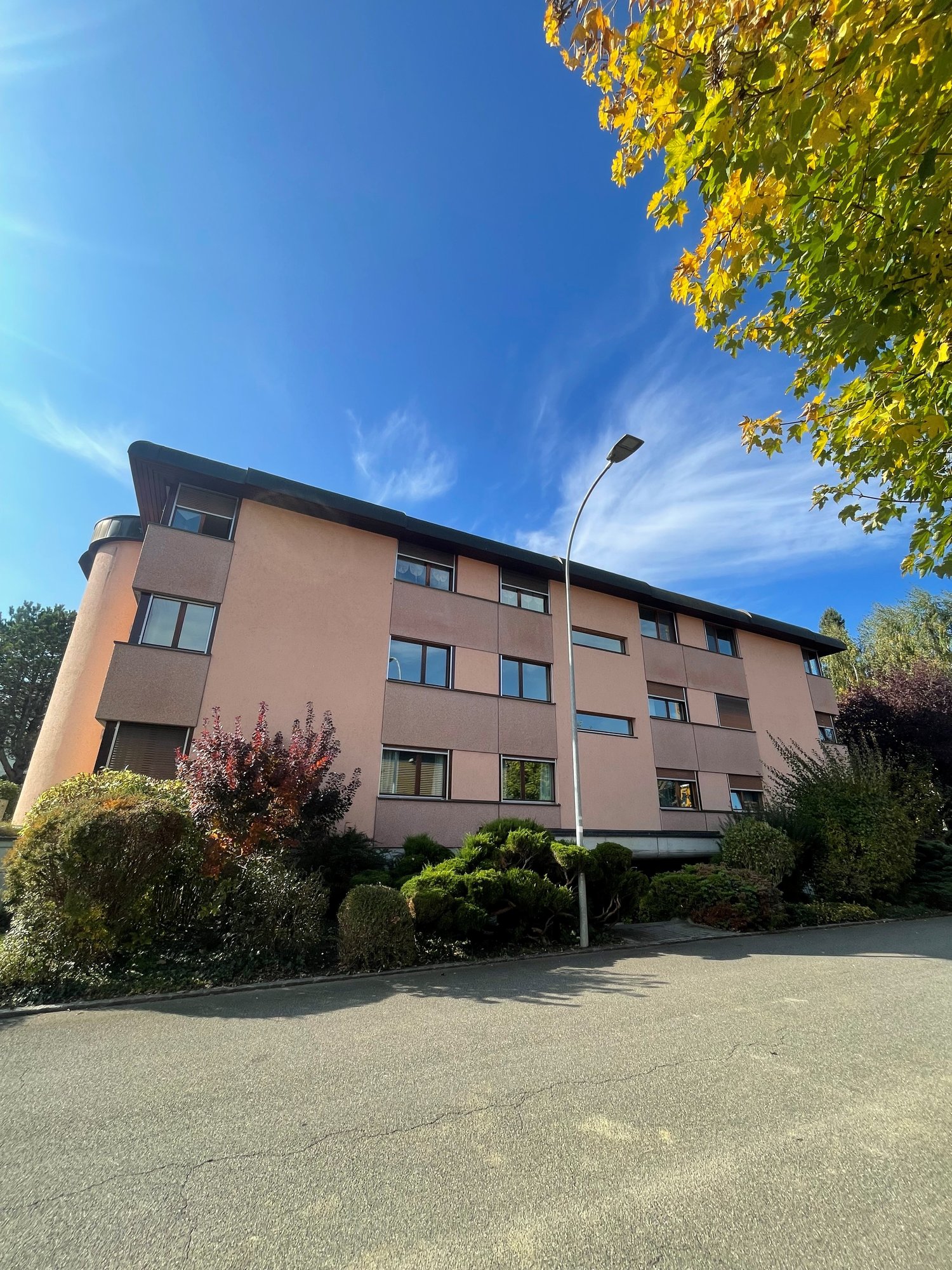 Multi-story apartment building, modern architecture, beige facade, large windows, street lamp, greenery