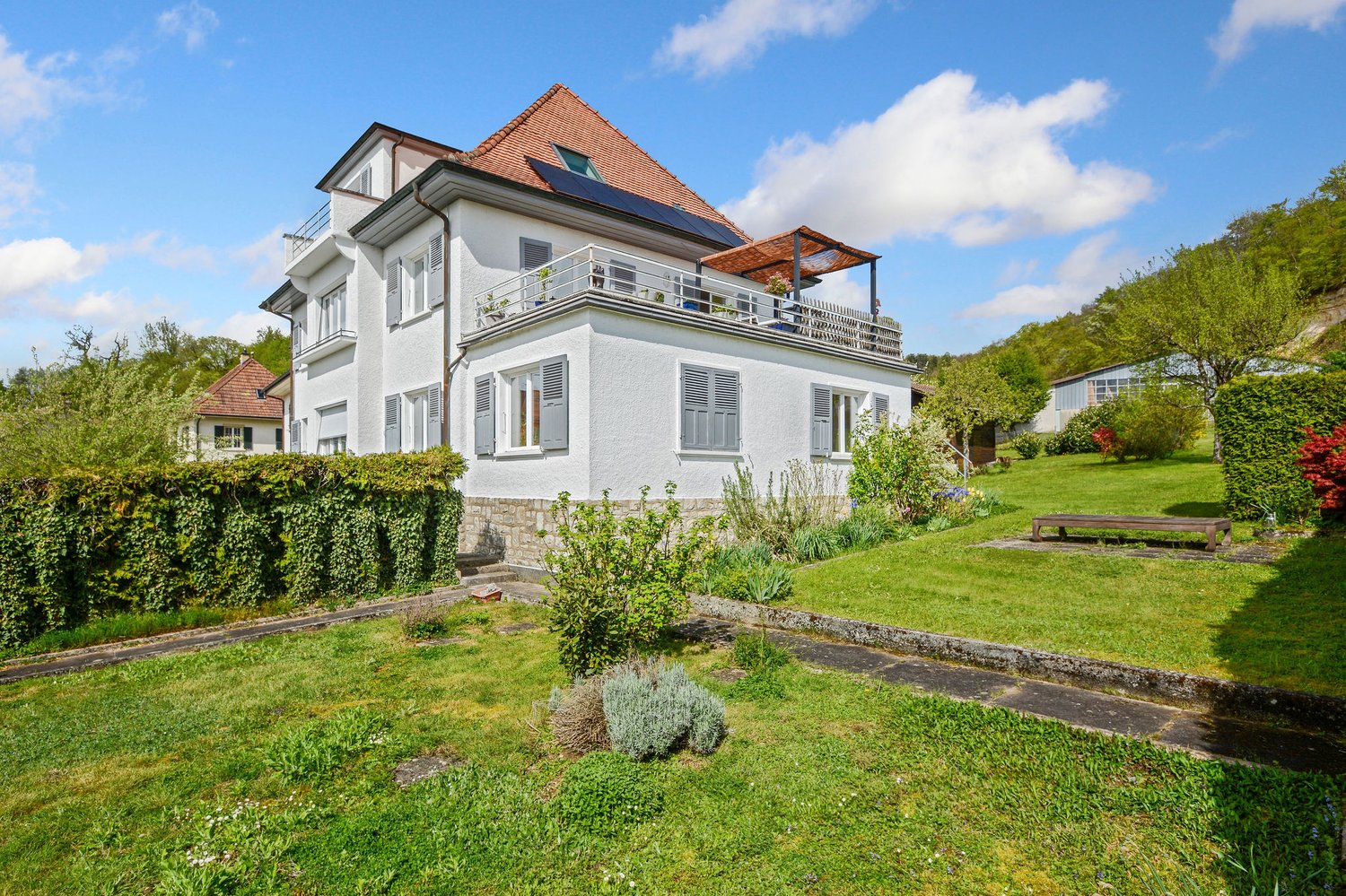2 story house, white exterior, brown roof, balcony, solar panels, garden, bench
