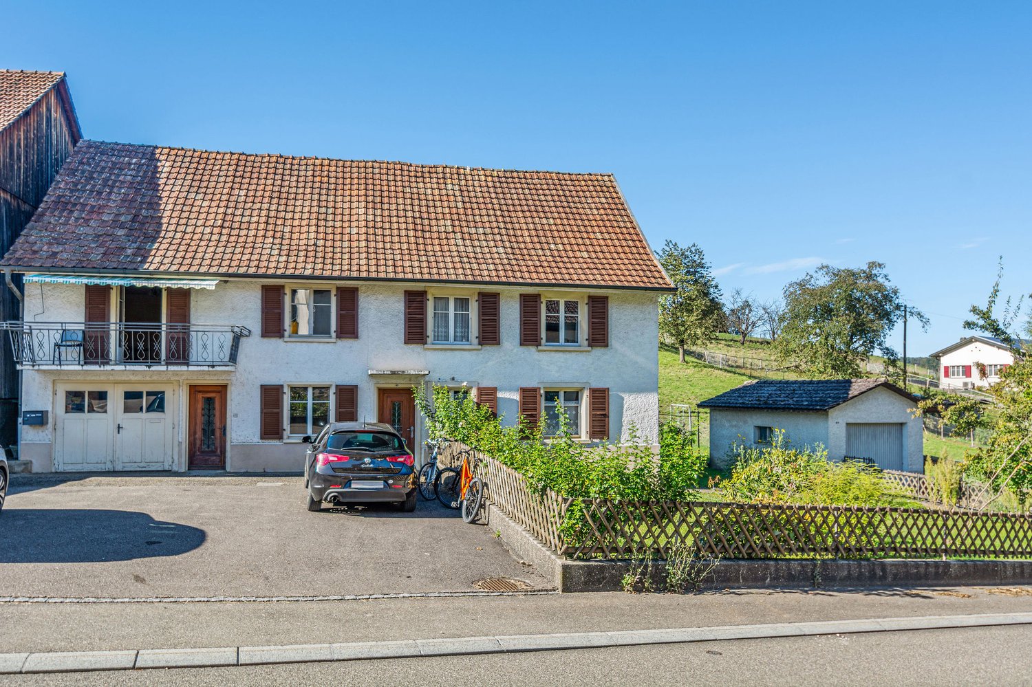Two-story house, brown roof, large windows, balcony, garage, two cars parked in driveway