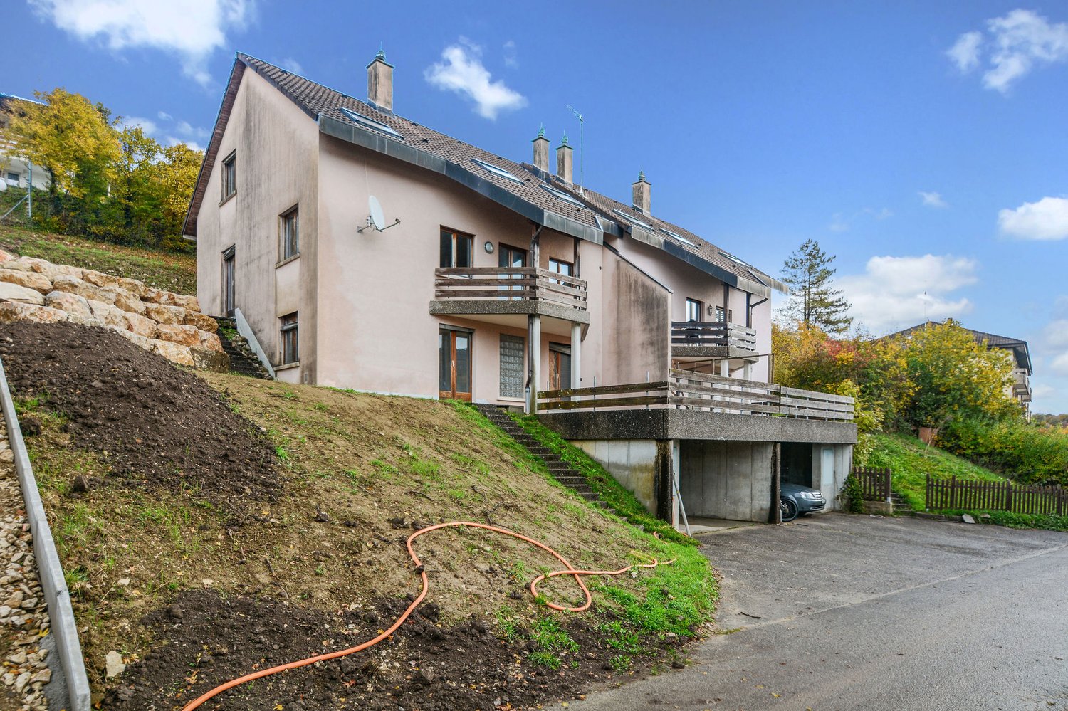 2 story house, pink facade, brown roof, balcony on second floor, satellite dish, driveway with garage