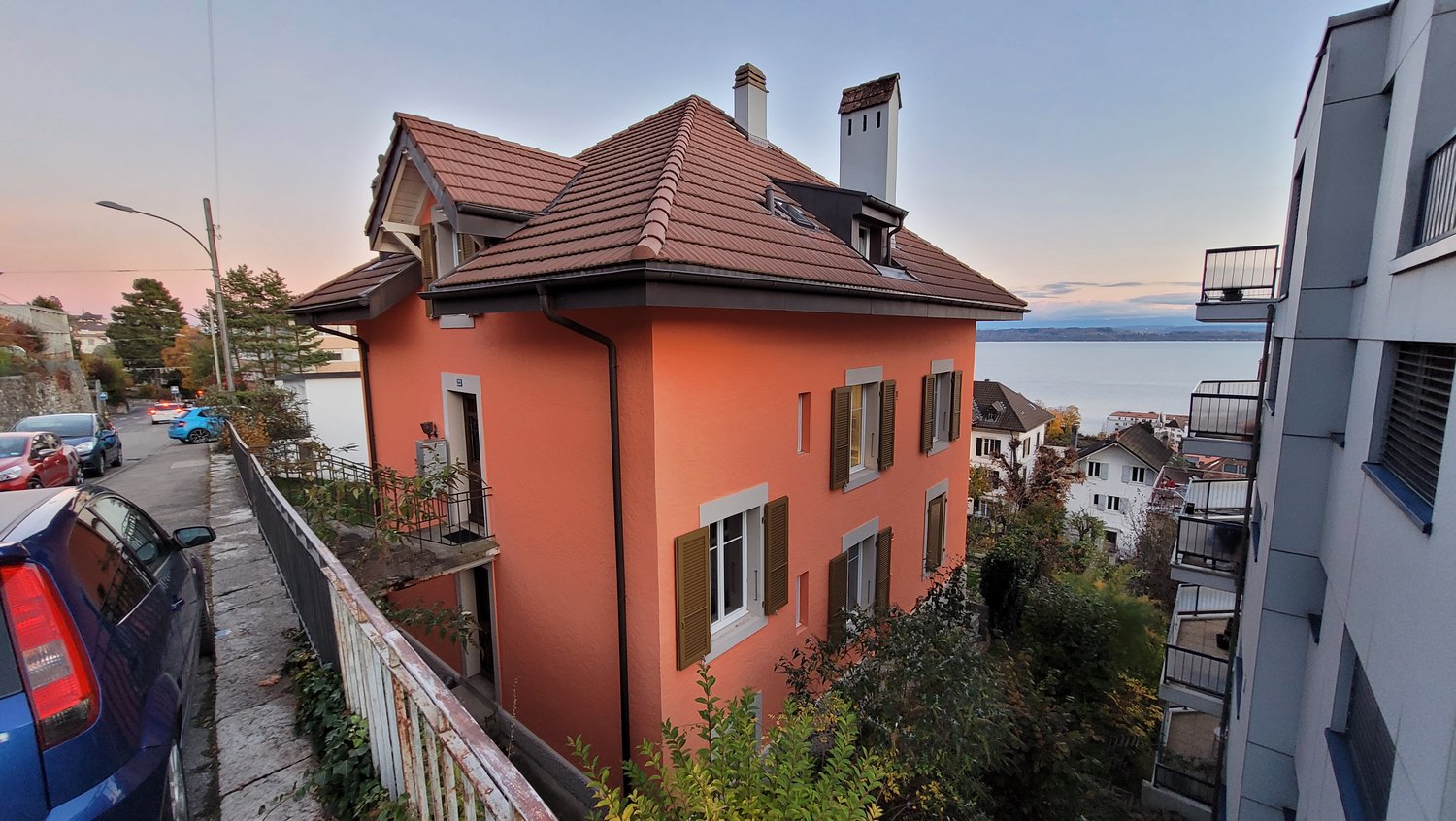 3 story house, red roof, orange walls, 2 chimneys, lake in background