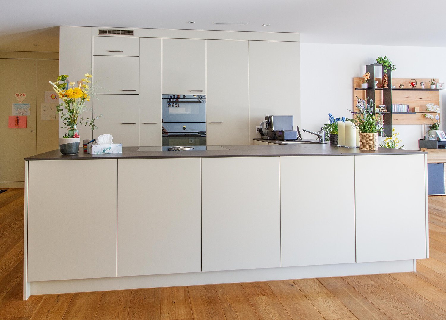 modern kitchen with white cabinetry, wooden flooring, integrated oven and stove, built-in sink, flower vase on counter