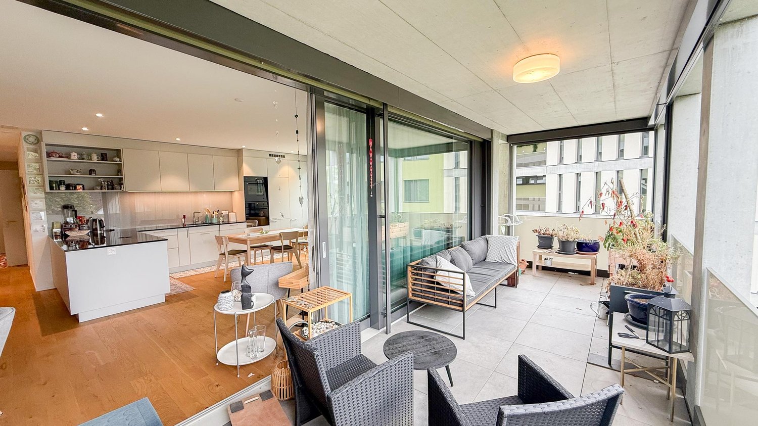 open plan living and dining area with kitchen, sliding glass doors leading to balcony, modern furniture, wooden floors, large windows, bright space