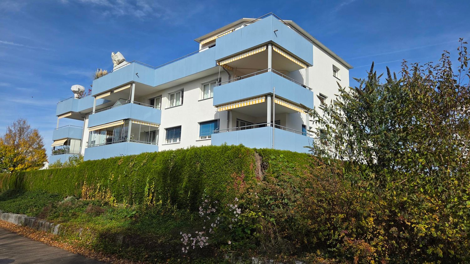 3 storey building with balconies, red roof, green hedges