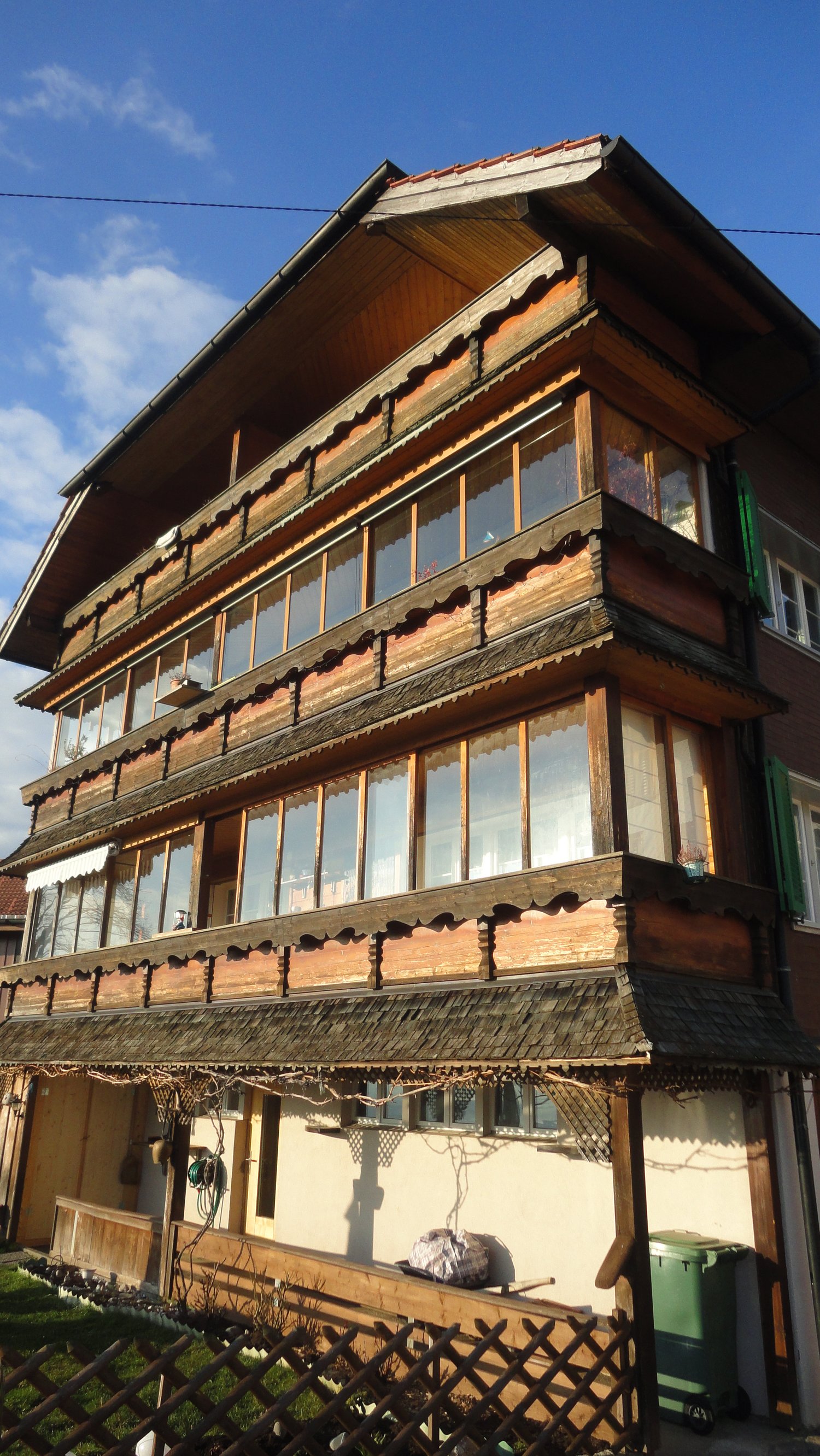 3 story house, wooden exterior, large windows, balcony, fence, small garden