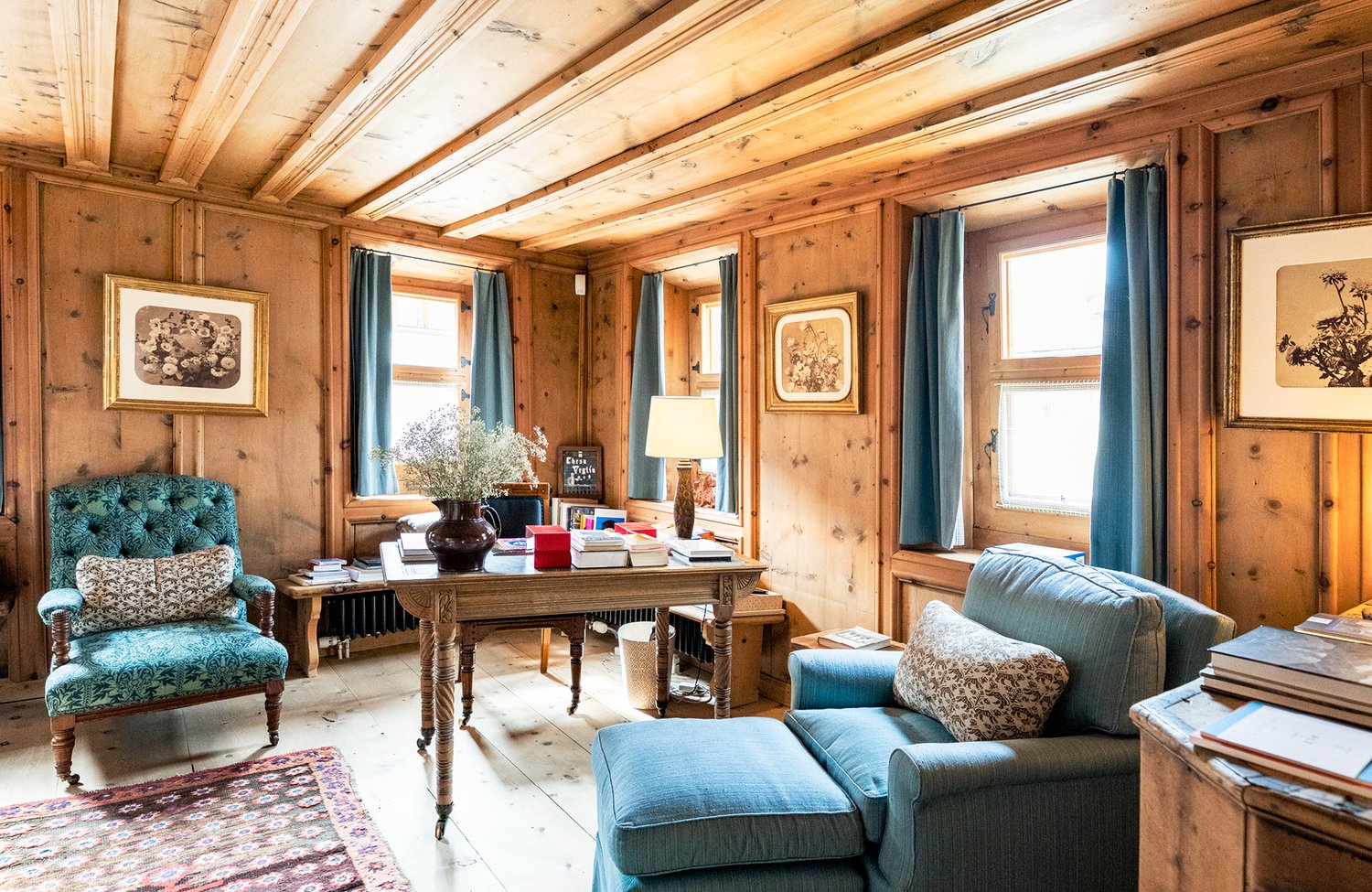 living room, wooden interior, desk, armchairs, carpet, bookshelf, framed pictures, lamp