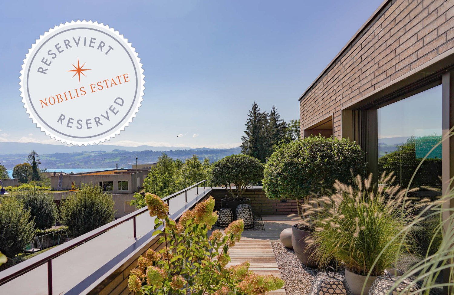 A terrace with railings, wooden deck, brick wall, potted plants, and a panoramic view of the surrounding landscape.