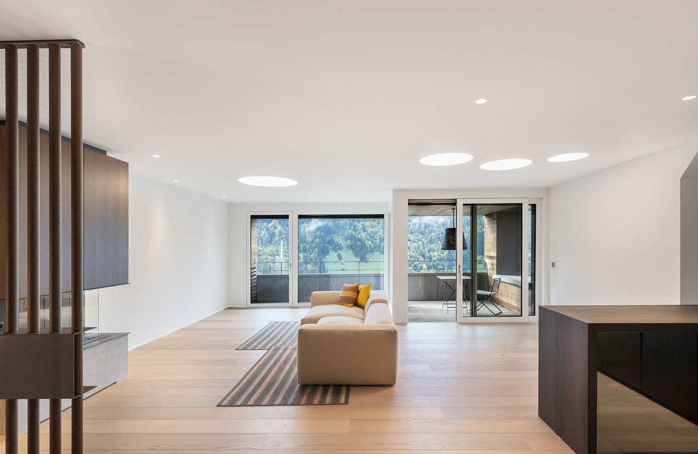modern interior, white walls, hardwood floors, beige couch, decorative pillows, large windows with balcony, circular lights