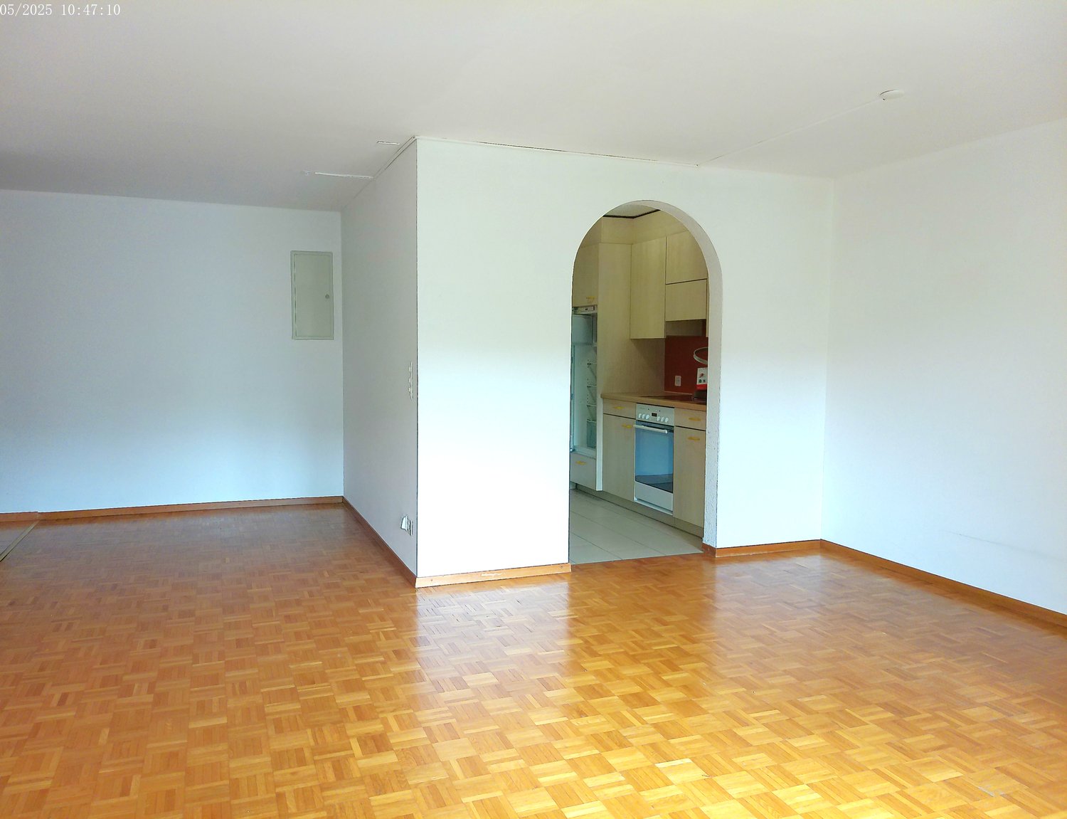 Open-concept living space with hardwood floors, white walls, and an arched entryway leading to the kitchen area with a visible dishwasher appliance.