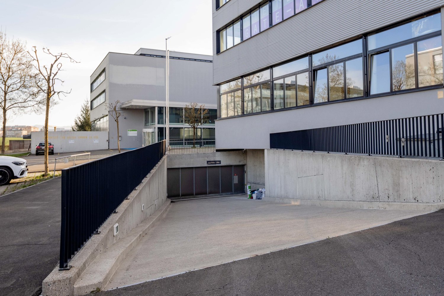 A modern, multi-story commercial building with large windows and a parking area in the foreground.