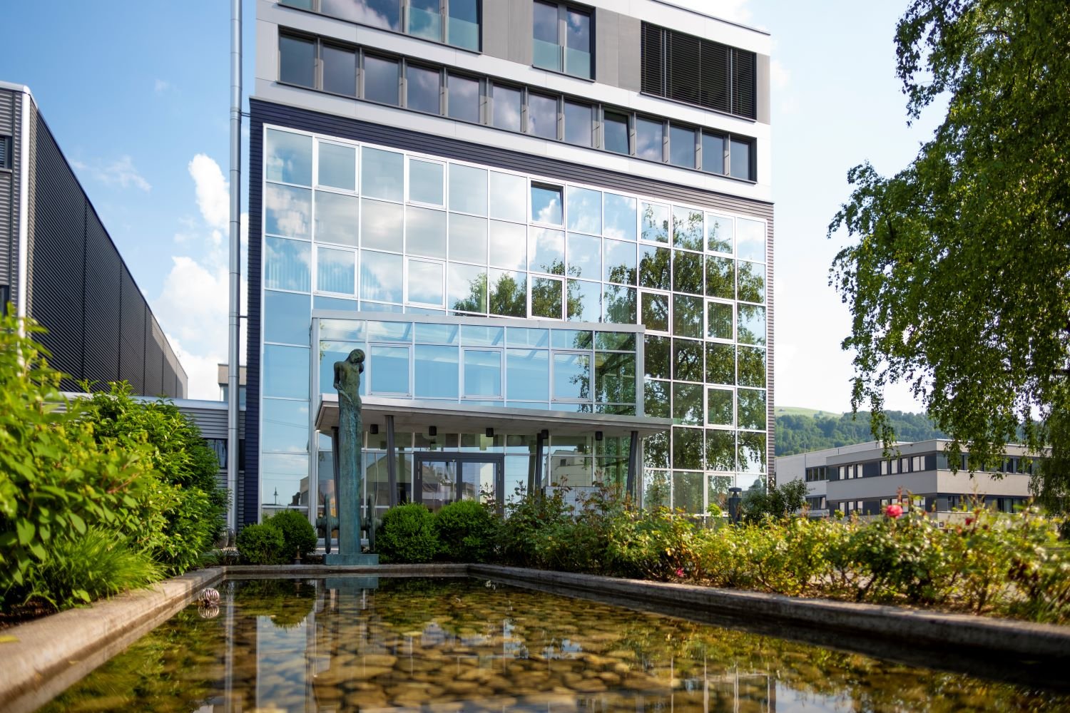 modern office building with glass facade, pond with sculpture in front