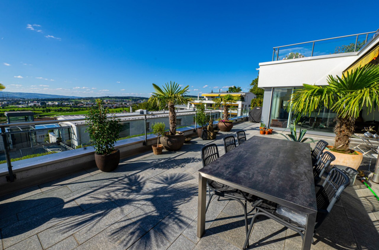 Stone floor, round table, chairs, palm trees, distant buildings, mountain range