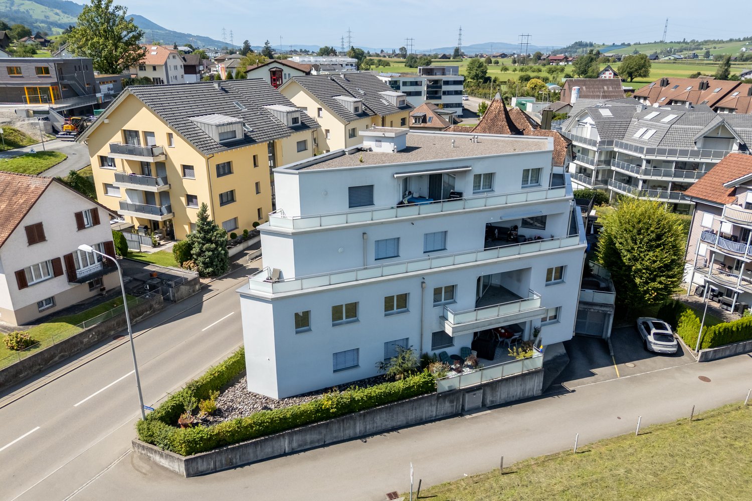 apartment building, white walls, multiple balconies, windows, car parked in front