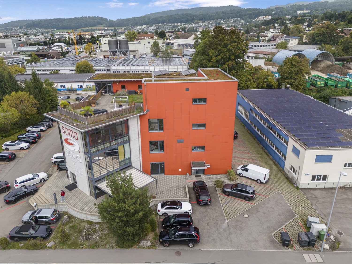 Industrial building with parking space in front, solar panels on the roof, orange facade, large glass windows
